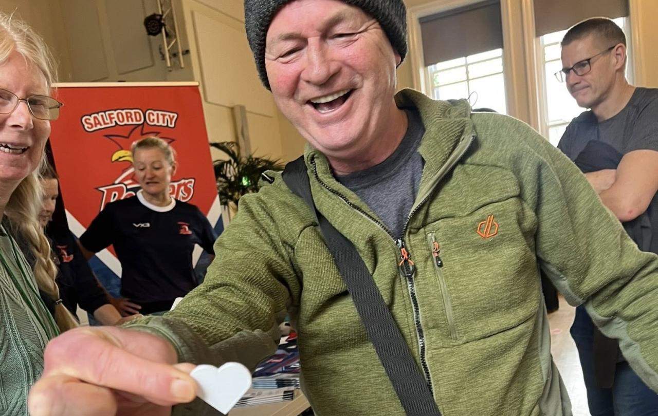 A man presents a heart shaped paper token towards the camera