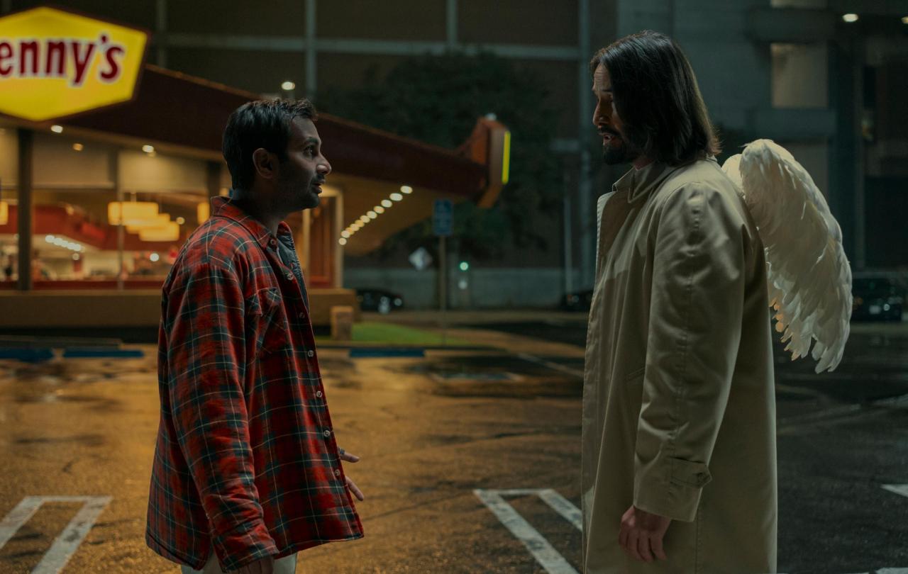 A film character talks to an angel in the street who has wings on the back of his coat.