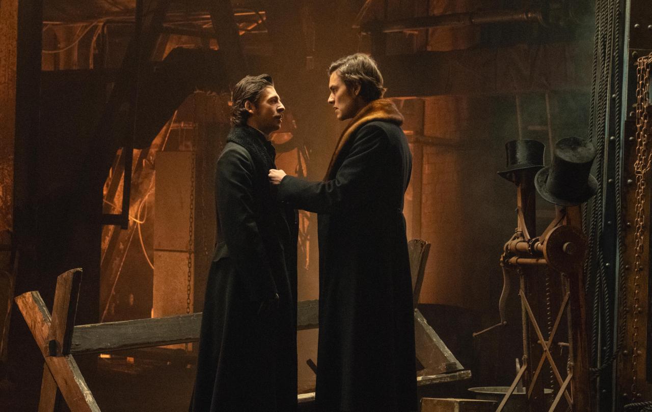 Two brothers look at each other in front of their ironworks.