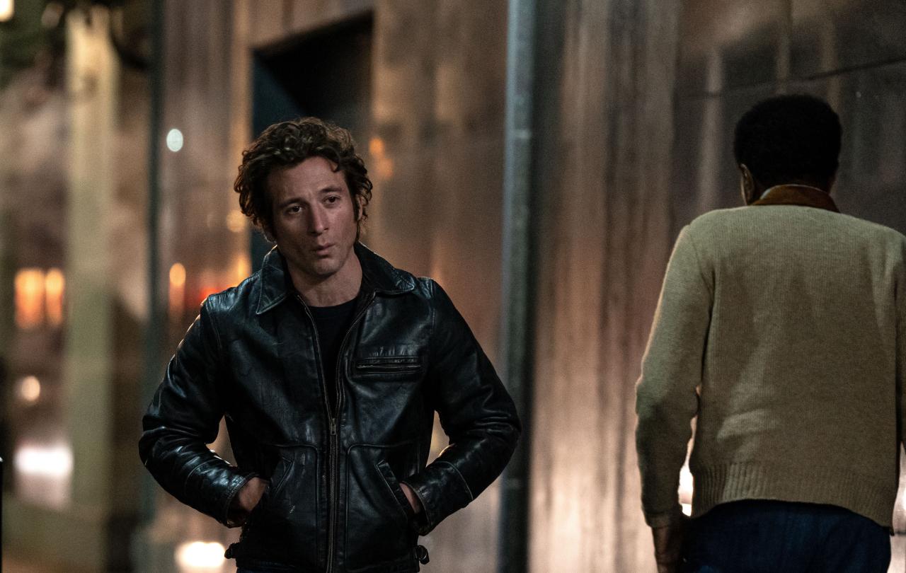 An actor playing Bruce Springsteen walks down a dark street, hands in jacket pocket.