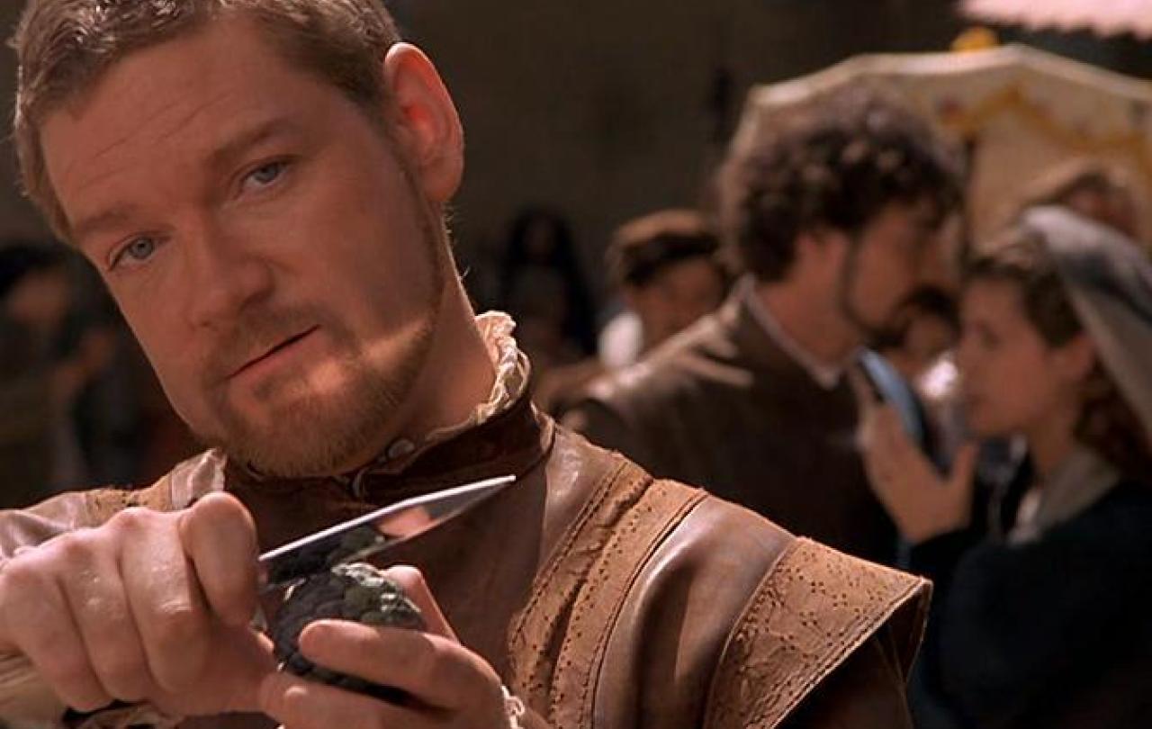An Elizabethan man holds a dagger up while grinning.