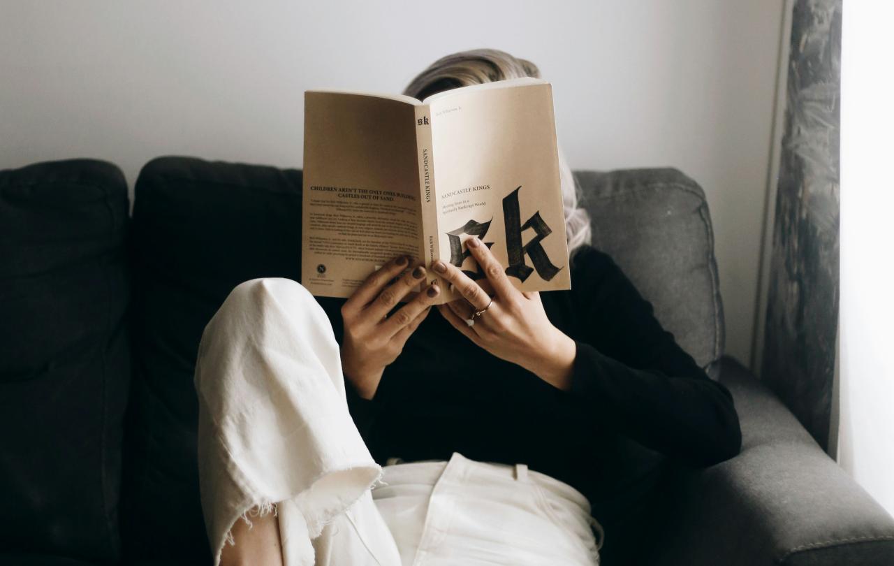   A reader sits on a sofa with a raised leg and holds a book
