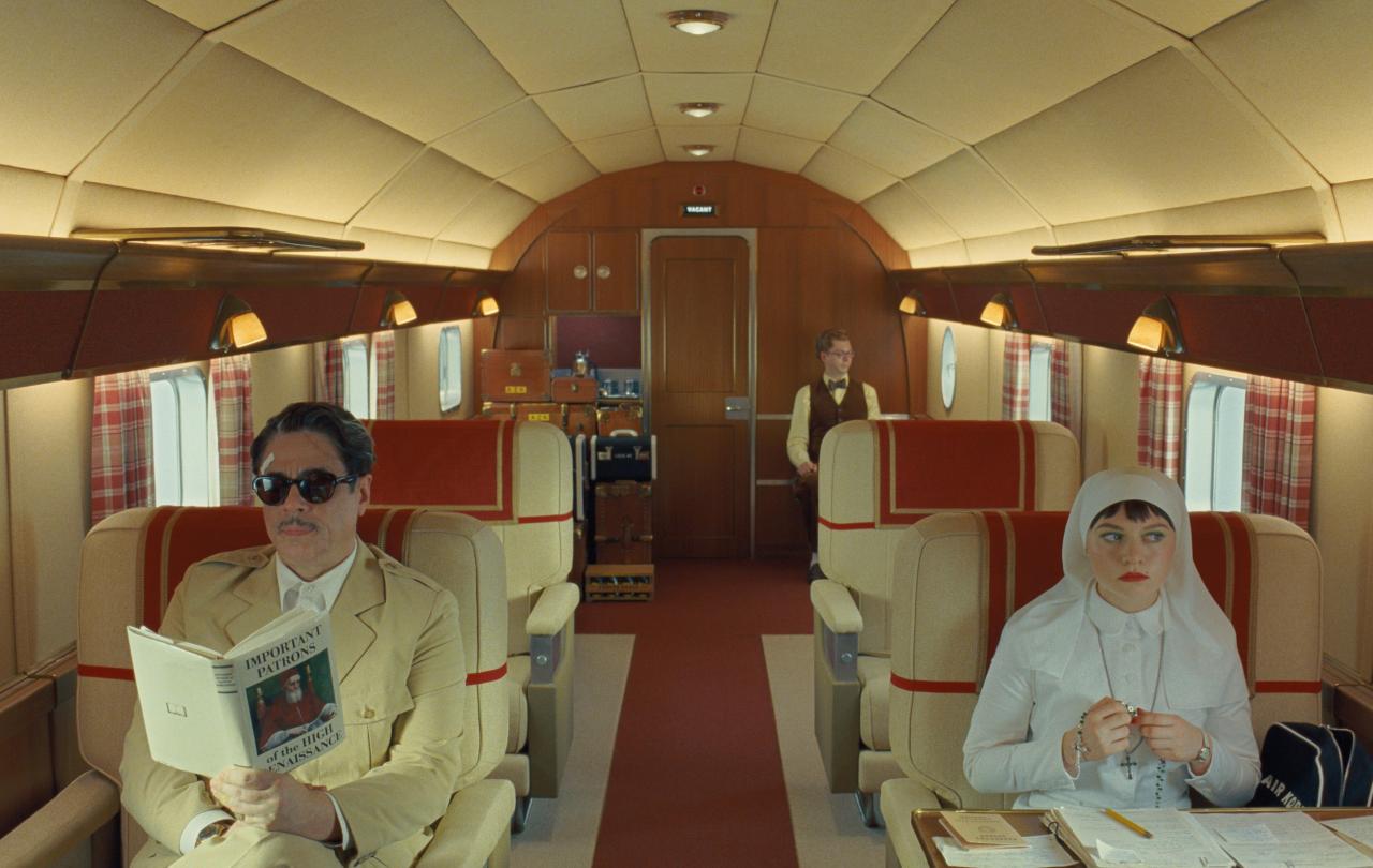 Characters from a Wes Anderson film sit in a stylish plane interior.