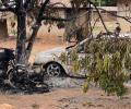 A burnt out motor cycle and car stand amid charred debris in a dusty compound.