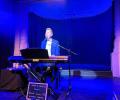 A pianist sits at a keyboard singing on a stage.