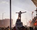 Amid celebrating football fans, one stands on top of a kiosk with outstretched arms.