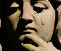 A stone statue's face depicts a falling tear.