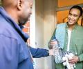 On a doorstep a man hands a bottle of water to another man.