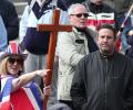 A protester wearing a Union Jack flag and hat and holding a cross, points while a man looks on.