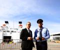 A prime minister stands next to an Albanian police officer in front of a ferry.