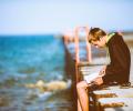 A man sits on a pier intently reading a book on his lap.