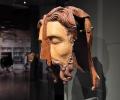 A split wooden sculpted head stands in an exhibition.