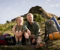 A hiking couple sit on the grass next to a pack.