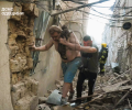 Amid a bombed alley, a victim is helped to walk by a rescue worker