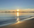 A sunset over an island casts golden light on the sea and a beach.