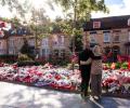 A couple hold each other as they look at floral tributes on the ground
