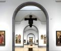 An art gallery arch reveals a suspended crucifix and other paintings in a distant room