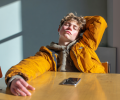 A seated teenager stretches back bored, a phone is on the table in front of them