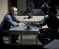 The Joker and Batman sit opposite each other in an interrogation room.