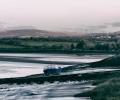 A boat rests on a mud bank of a river, hills are in the background.