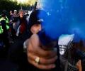 A protestor holds a blue smoke canister towards the camera lens.