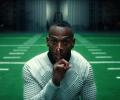 A player holding a finger to his lips stands in front of an indoor American football pitch.