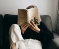   A reader sits on a sofa with a raised leg and holds a book