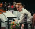A seated Celine Dion, leans forward, head to the side, holding a mic.
