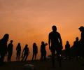 A setting sun back-lights a crowd of young people on a beach
