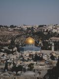 A blue and gold domed mosque sits surrounded by old stone buildings of a city.