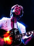 A singer holding a guitar raises his head with closed eyes.