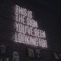 A white neon sign against a brick wall reads: 'This is the sign you have been looking for.