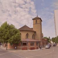 A neo-Romanesque church sits at the acute corner of two roads. To its side a tower block rises over a row of low-rise flats.