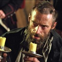A desperate man wearing 18th century clothes holds candlesticks