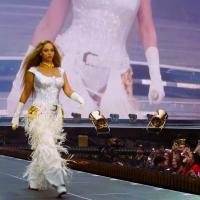 Beyonce marches along a stage catwalk as photographers stare from below.