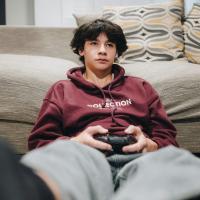 A teenager slumped against a sofa plays a video game