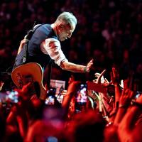 Bruce Springsteen crouches down and holds a hand out to a sea of outstretched hands