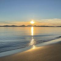 A sunset over an island casts golden light on the sea and a beach.