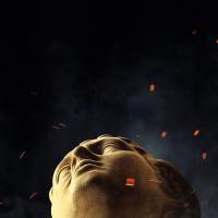 the head of a classical statue looks up amid embers around it.