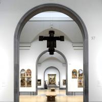 An art gallery arch reveals a suspended crucifix and other paintings in a distant room