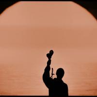 A silhouette of a musician holding up shakers.