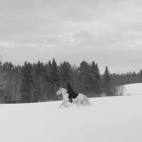 A nun on a white horse, gallops across a snowy field, in black and white