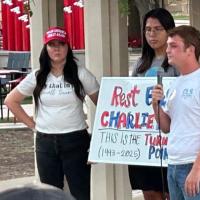 Mourning students at a vigil hold a sign about Charlie Kirk.