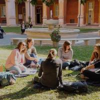 Students sit on the grass in front of a fountain.