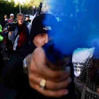 A protestor holds a blue smoke canister towards the camera lens.