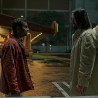 A film character talks to an angel in the street who has wings on the back of his coat.