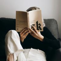   A reader sits on a sofa with a raised leg and holds a book