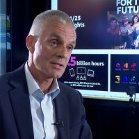 TIm Davie, sits in an interview in front of screens showing facts about the BBC