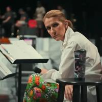 A seated Celine Dion, leans forward, head to the side, holding a mic.