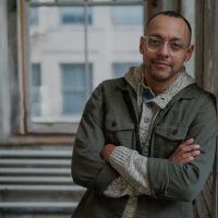A man leans against a wall, arms folded.